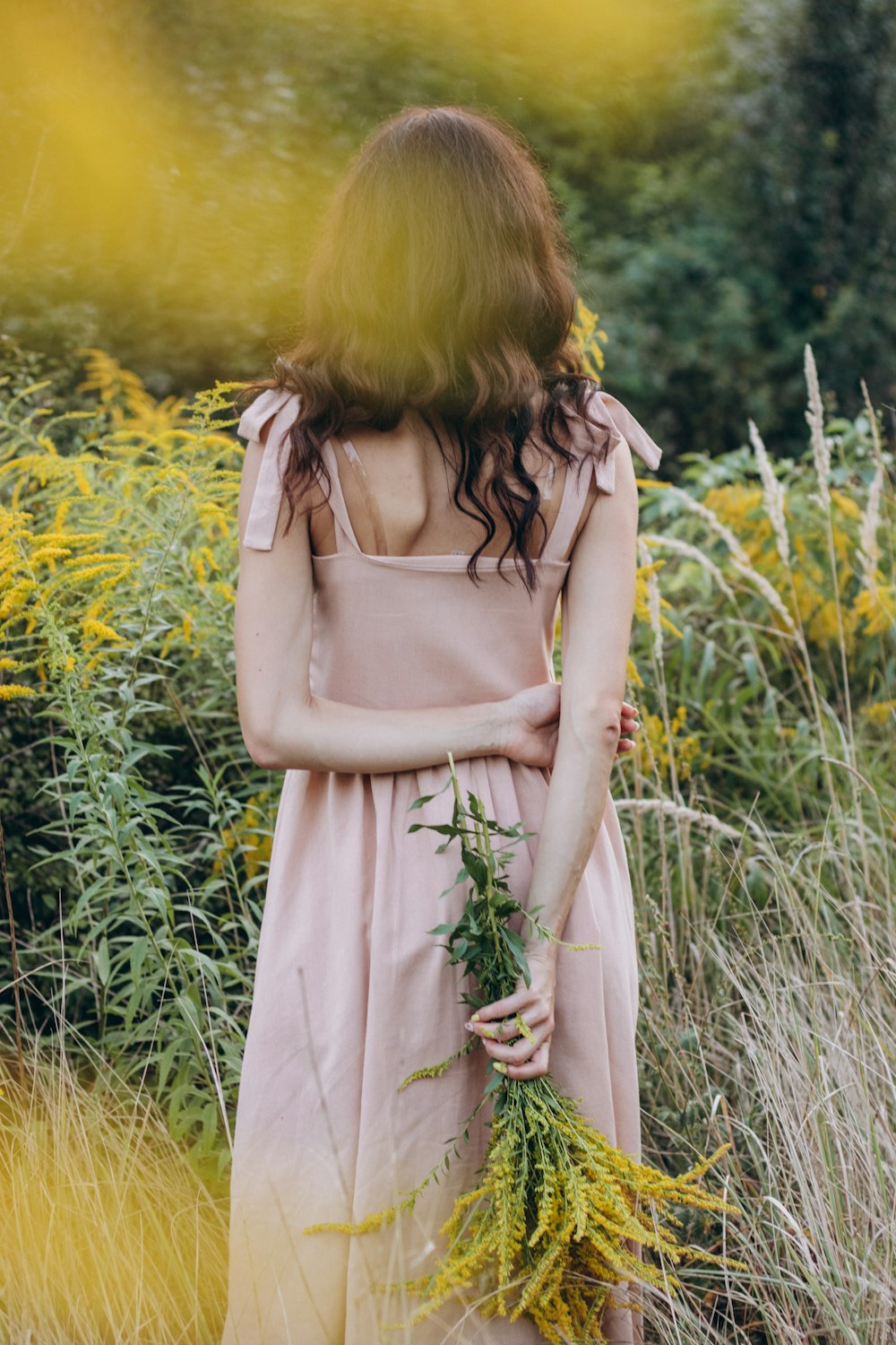 a woman in a pink dress standing in tall grass