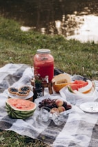 a picnic with watermelon, grapes, melon, and a jar of