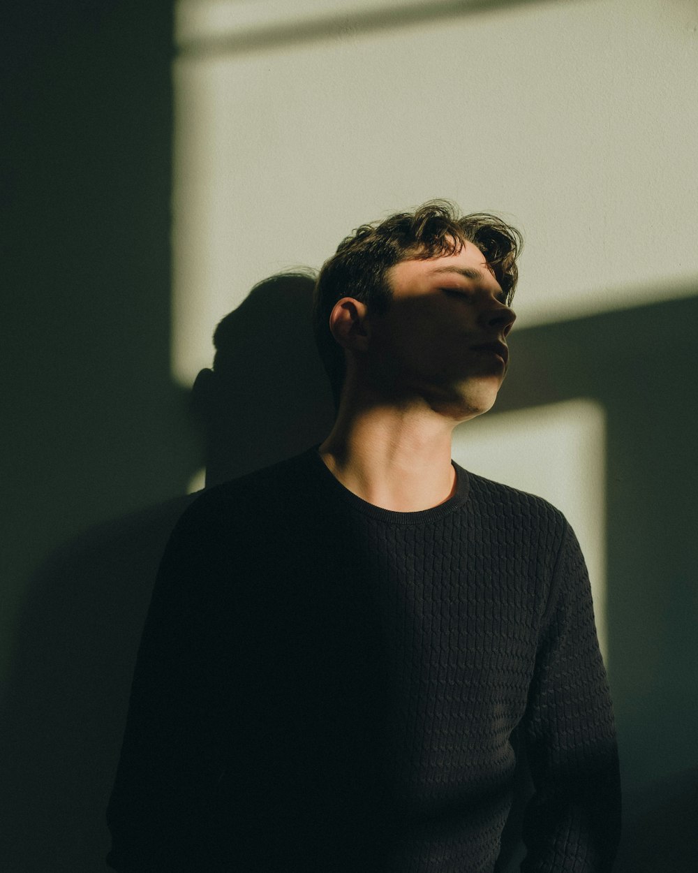 a man standing in front of a wall with his eyes closed