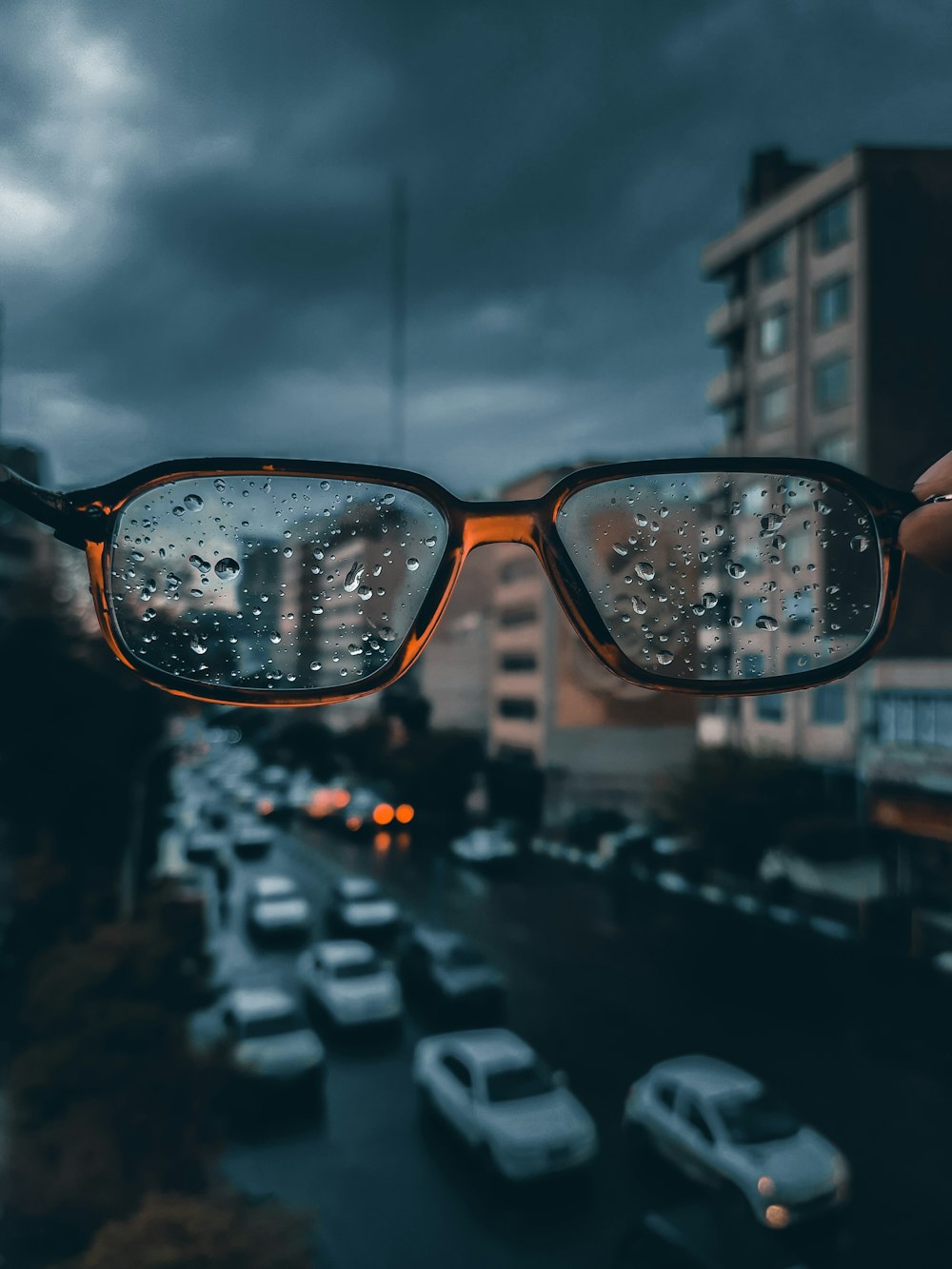 a person holding up a pair of glasses with rain drops on them