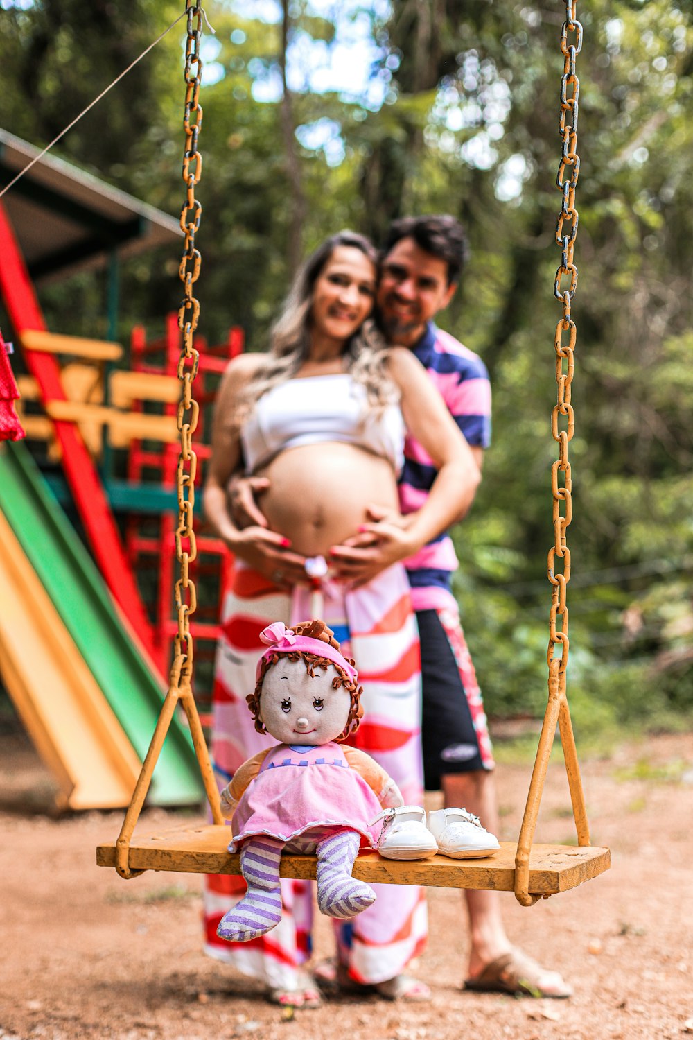 a pregnant woman sitting on a swing with a baby doll