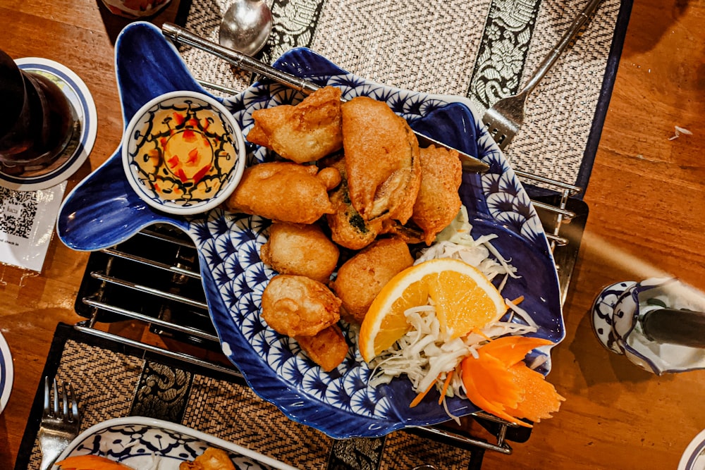 a blue plate topped with fried food next to a bowl of dipping sauce