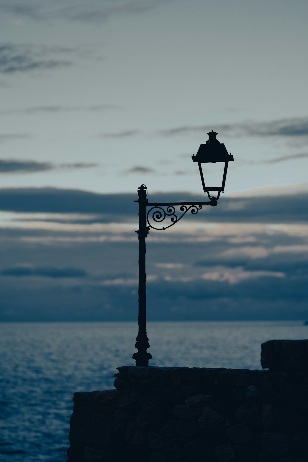 a street light sitting on top of a stone wall next to the ocean