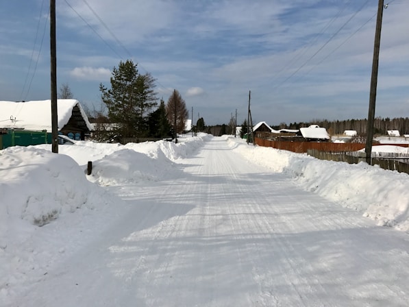 a road that is covered in snow with houses in the background