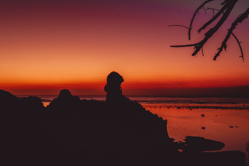 une silhouette d’une personne assise sur un rocher au coucher du soleil