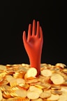a pile of gold coins with a red hand sticking out of it