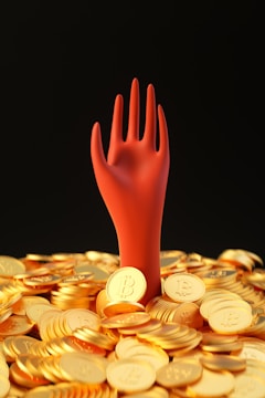 A stylized red hand emerges from a pile of shiny golden coins, each marked with the Bitcoin symbol, against a dark background.