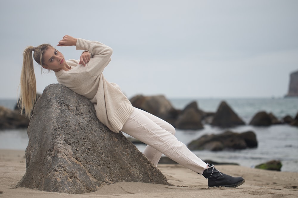 a woman sitting on top of a rock on a beach