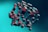 A collection of three-dimensional cubes is suspended in mid-air against a gradient teal background. The cubes vary in size and orientation, creating a dynamic and abstract pattern. The interplay of light and shadow on the cubes gives them a metallic appearance with hints of red and blue.