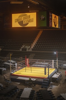 a wrestling ring in an empty arena with a man standing on it