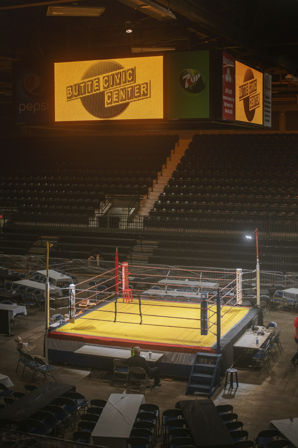 a wrestling ring in an empty arena with a man standing on it