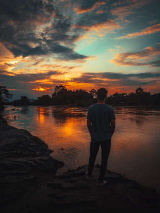 a man standing on the edge of a river watching the sunset