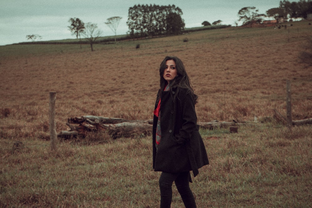 a woman standing in a field in a black coat