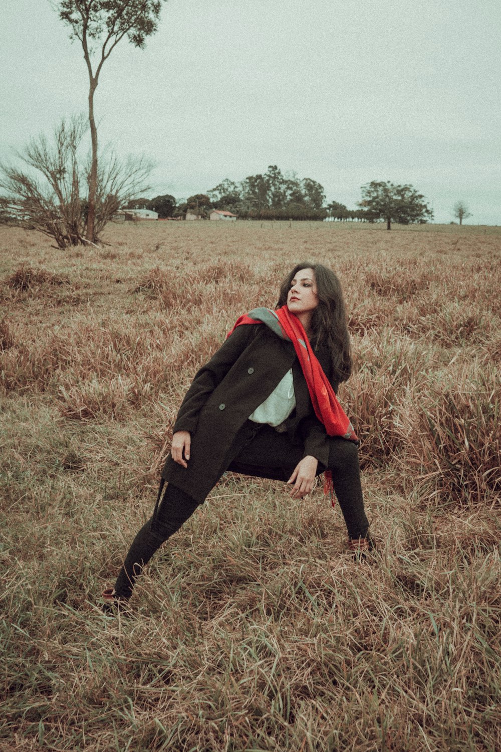 a woman sitting in a field with a red scarf around her neck