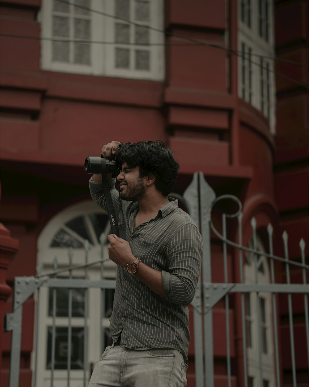um homem segurando uma câmera na frente de um edifício vermelho