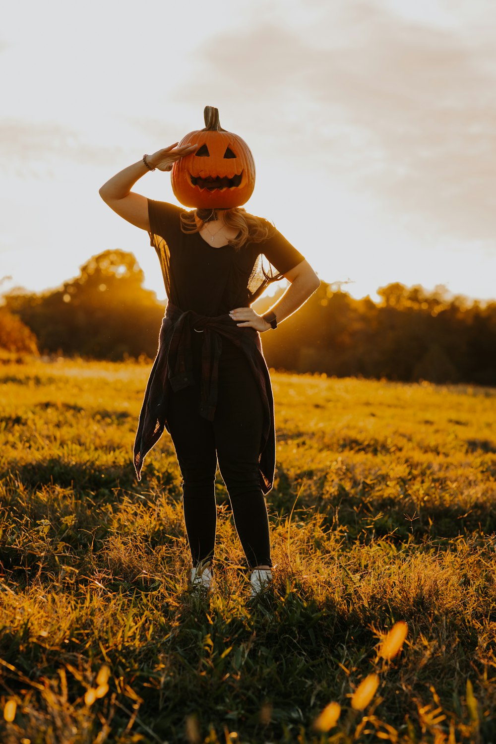 a woman standing in a field with a pumpkin on her head