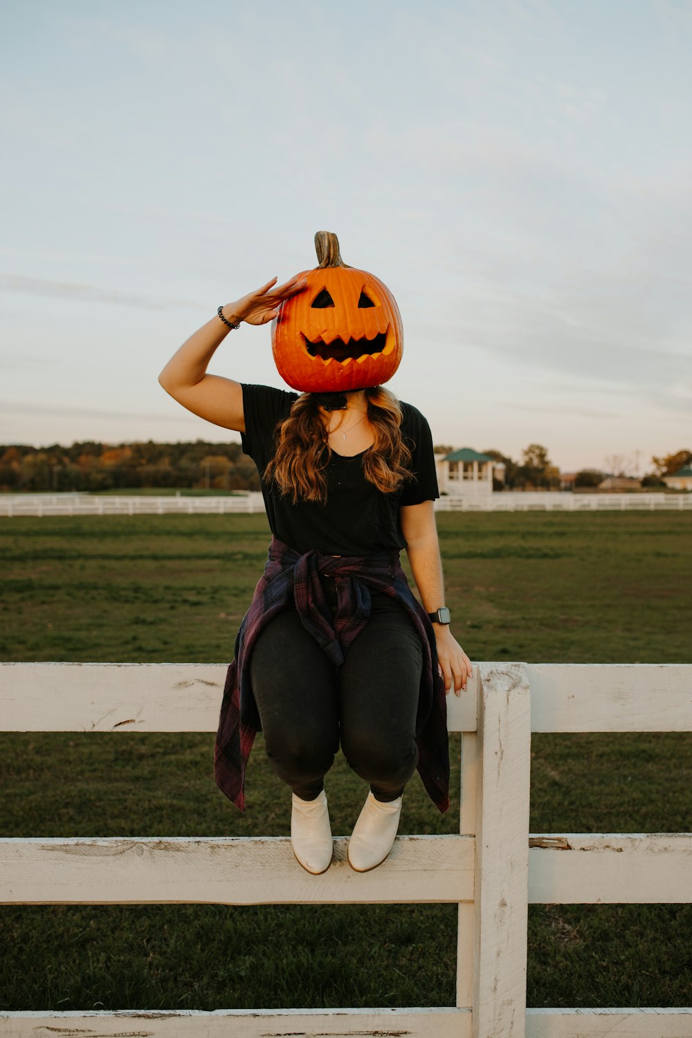 a woman sitting on a fence with a pumpkin on her head