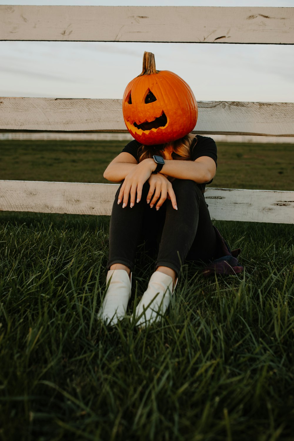 a woman sitting in the grass with a pumpkin on her head