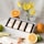 A display of four boxed fragrances set in a white tray, surrounded by fresh citrus fruits including oranges, lemons, and limes. Yellow flowers in a glass vase add a touch of freshness, and the background is a light, textured fabric.