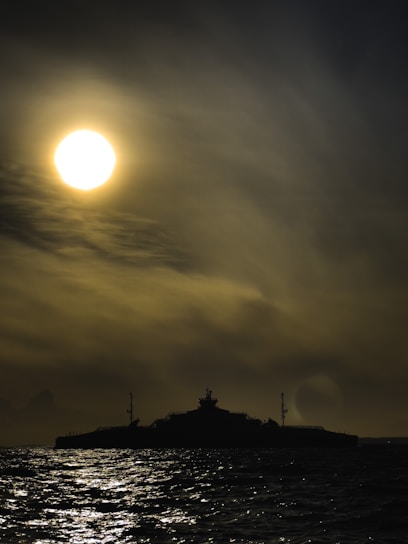 A dramatic battleship cutting through deep blue ocean waves under a cloudy sky.