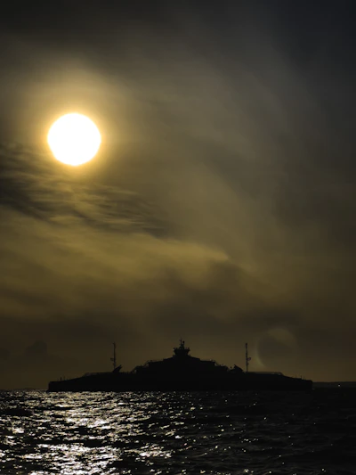 A dramatic silhouette of the USS Nimitz cutting through dark ocean waters under a stormy sky.