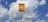 A yellow sign with black text in Portuguese stands against a backdrop of a blue sky with scattered white clouds. The sign appears to be a warning about an underground gas pipeline, advising not to dig. It is mounted on a tall metal pole.