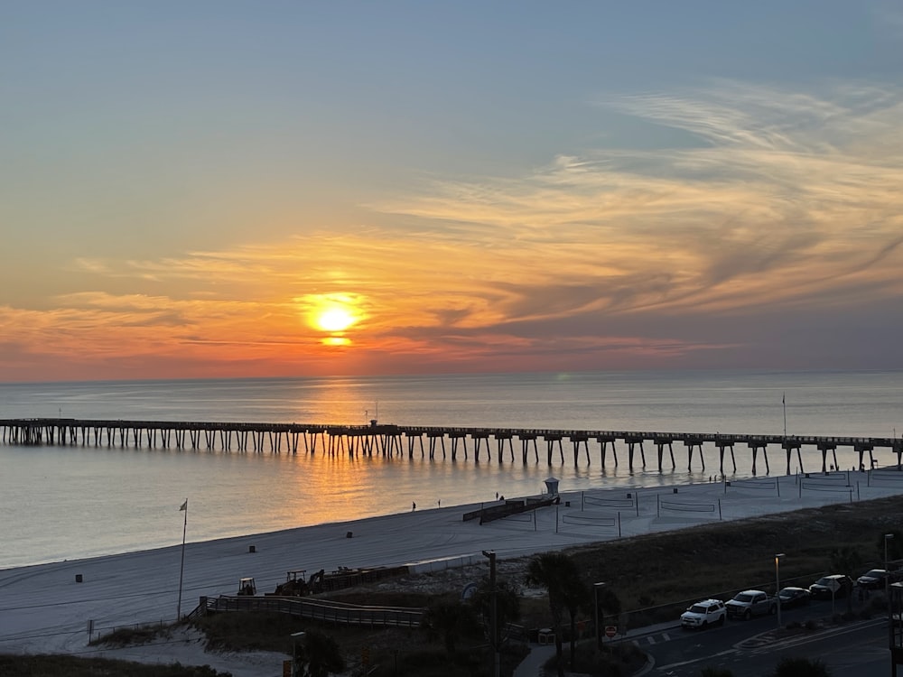 the sun is setting over the ocean with a pier in the distance