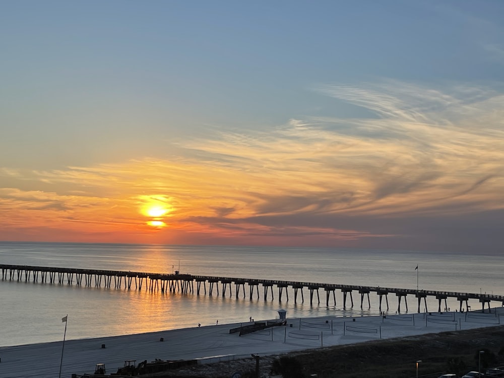 the sun is setting over a long pier