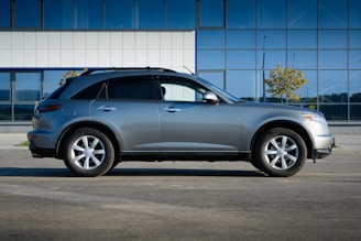 Glossy silver SUV parked in front of a modern glass building on a sunny day.