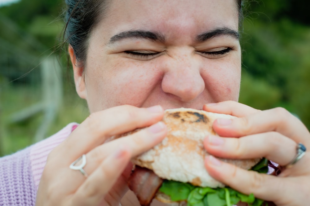 a woman biting into a sandwich with lots of lettuce
