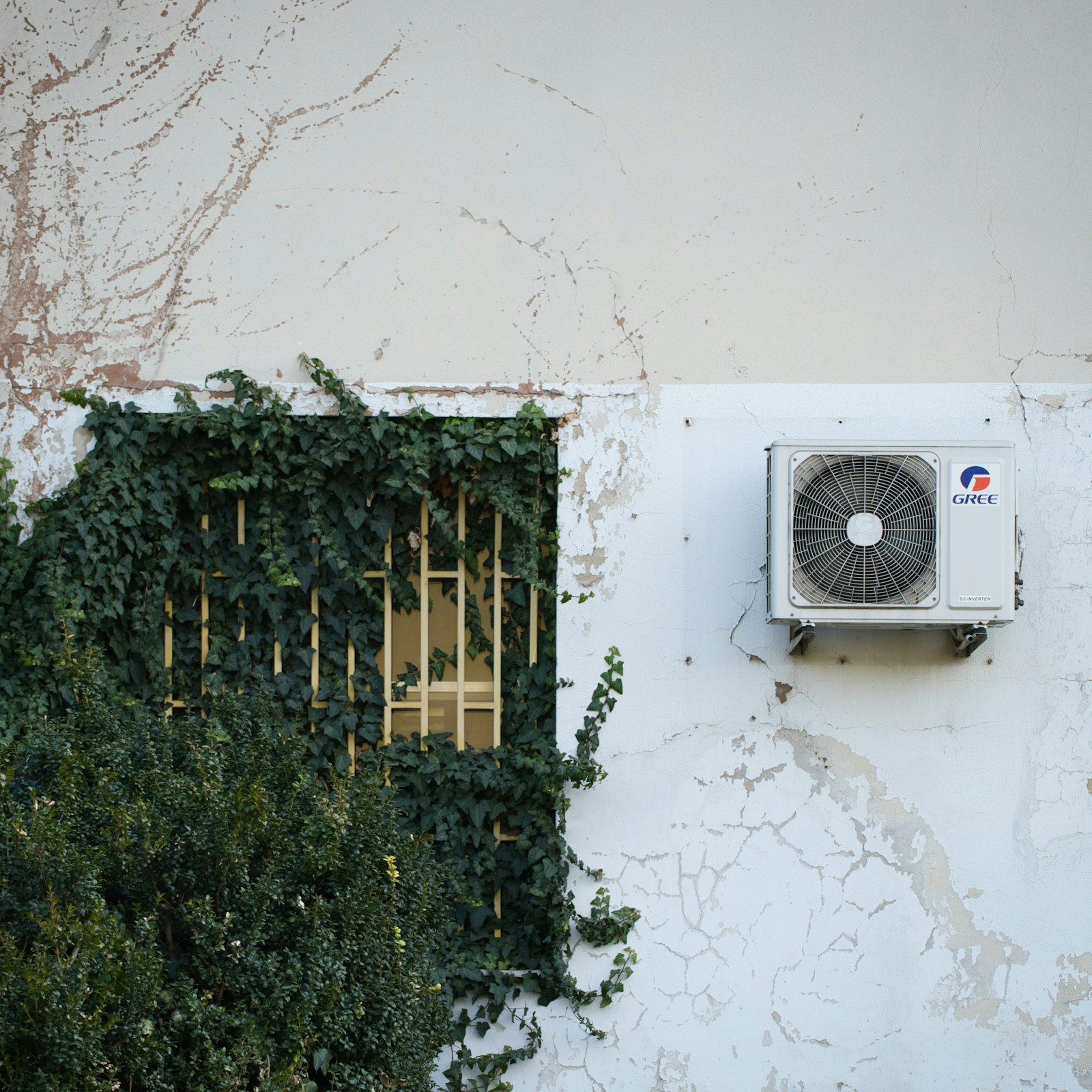 Outdoor air conditioning condenser unit mounted on a sunlit home exterior wall, representing a seasonal AC maintenance visit