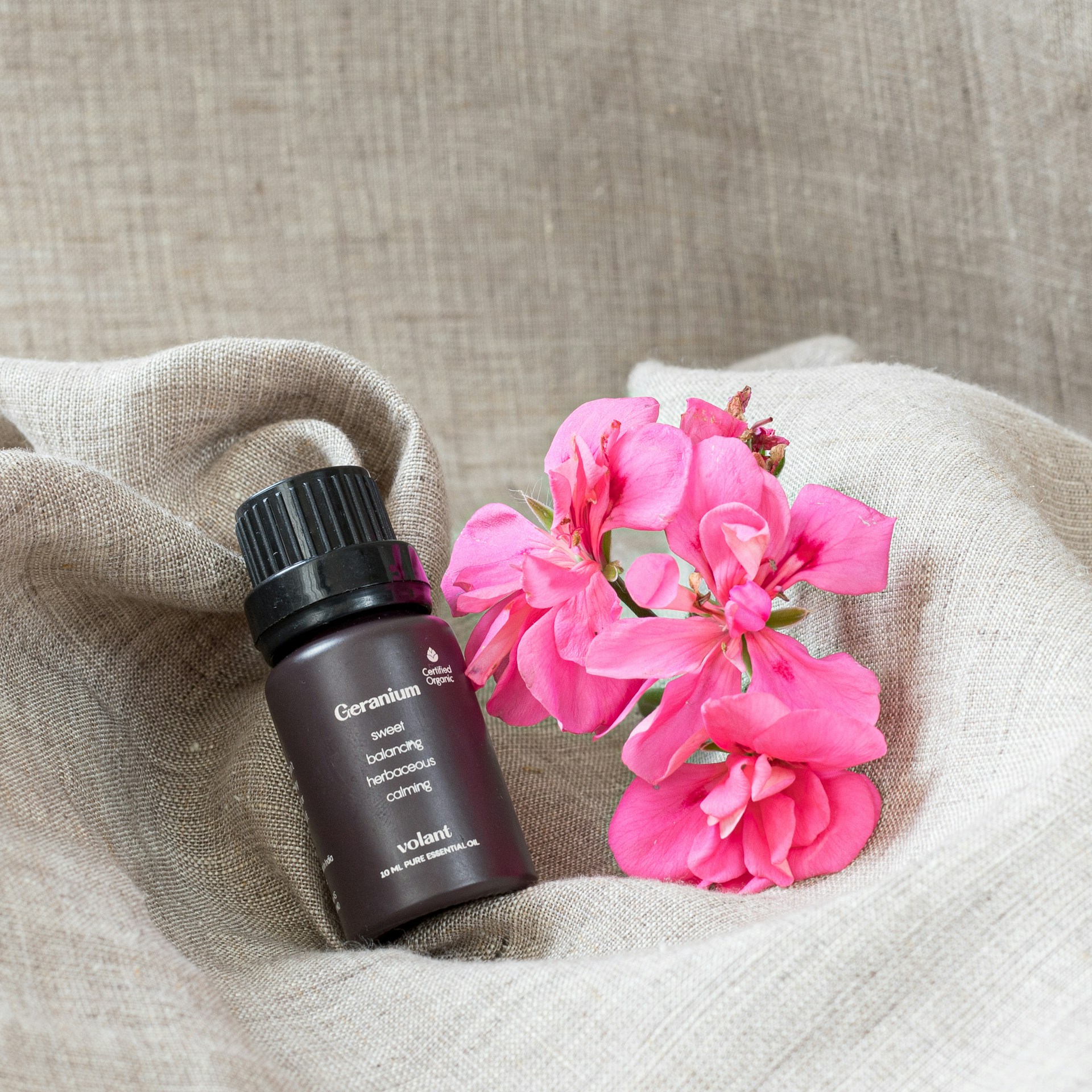 a bottle of essential oils next to a pink flower
