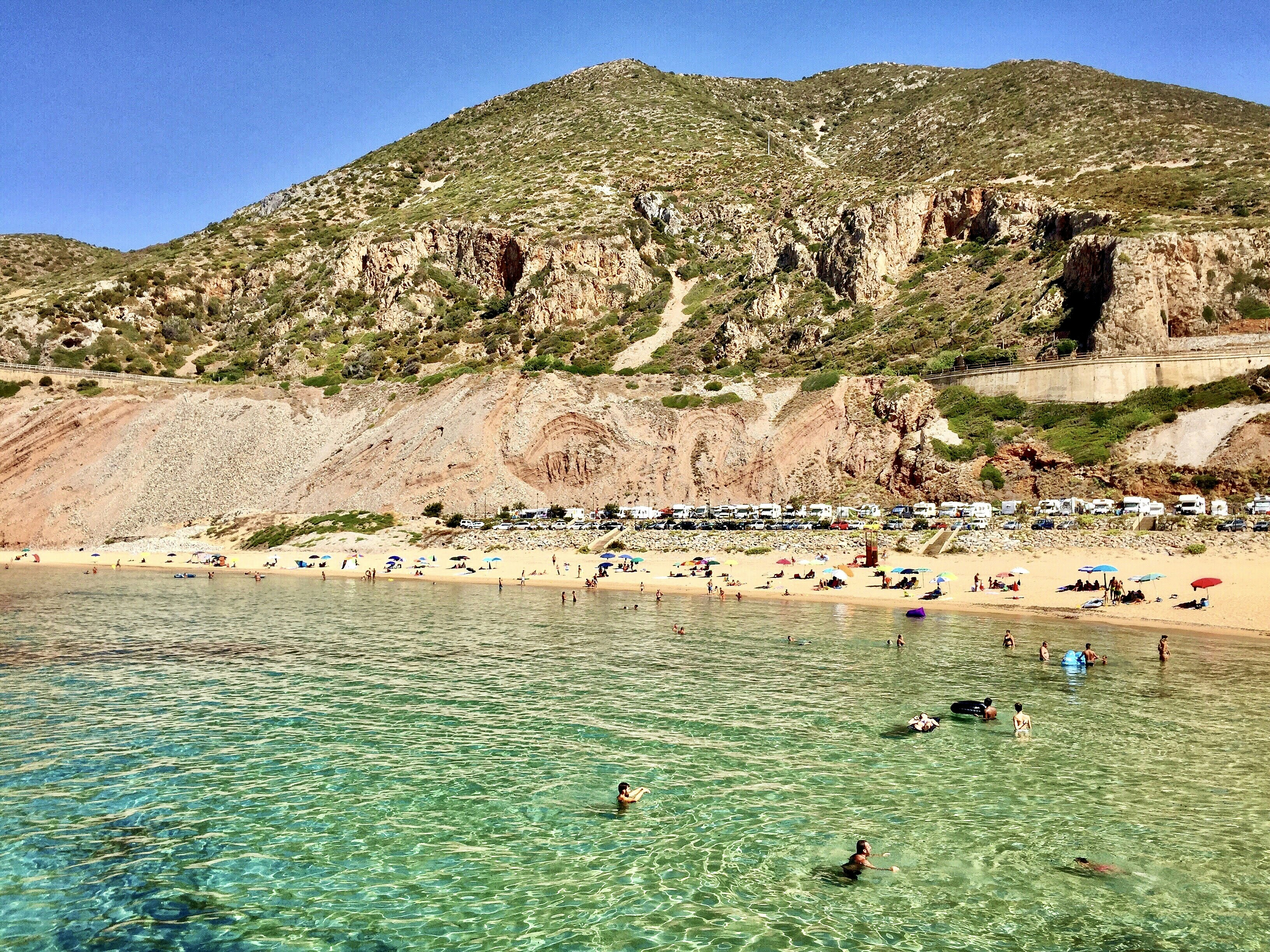 a group of people swimming in a body of water, Buggerru beach, Sardinia, Italy 