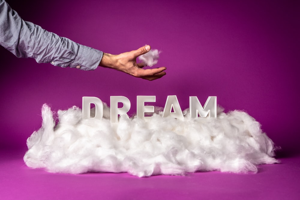 a hand reaching for a cloud of cotton on a purple background