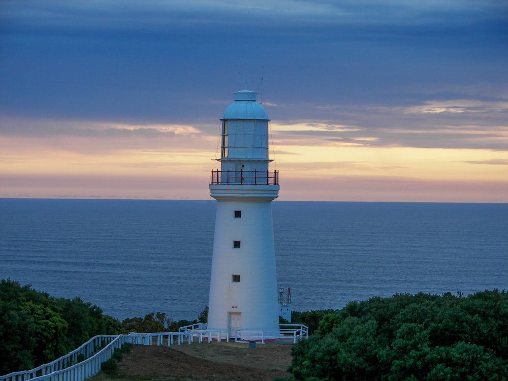 a white lighthouse sitting on top of a hill next to the ocean