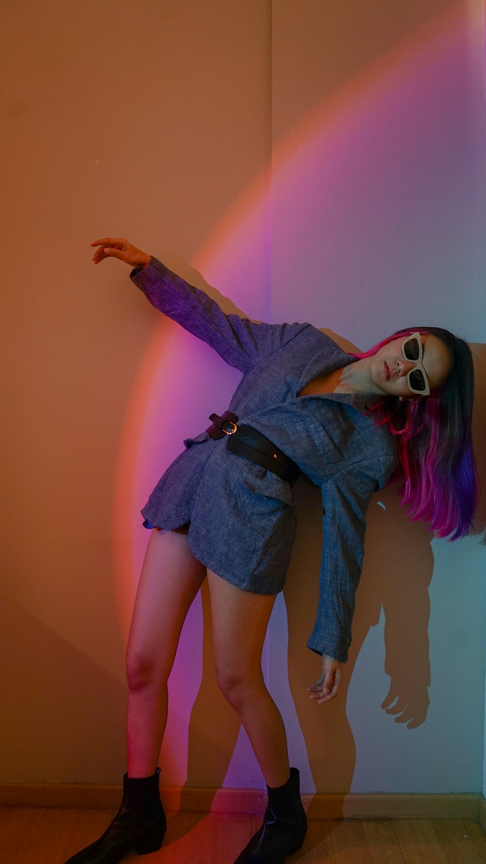 a woman with pink hair and sunglasses leaning against a wall