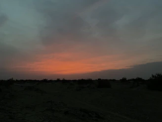 Documentary-style photo of a serene desert sunrise with soft pink, purple, and orange hues over a peaceful retreat setting.