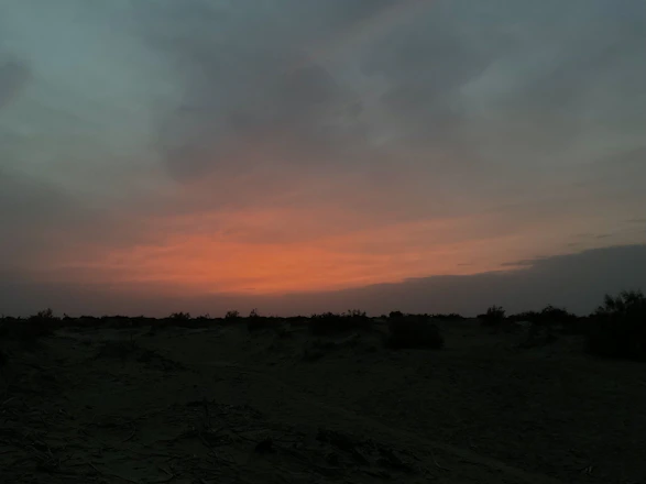 Documentary-style photo of a serene desert sunrise with soft pink, purple, and orange hues over a peaceful retreat setting.