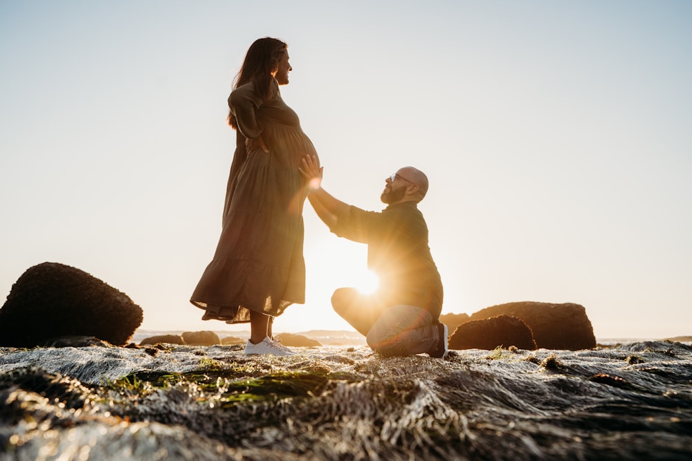 a man kneeling down next to a woman on top of a body of water