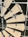 A close-up view of a windmill style ceiling fan with wooden blades. The fan blades are attached to a central hub with black brackets. The background shows the metal framework of a ceiling grid.