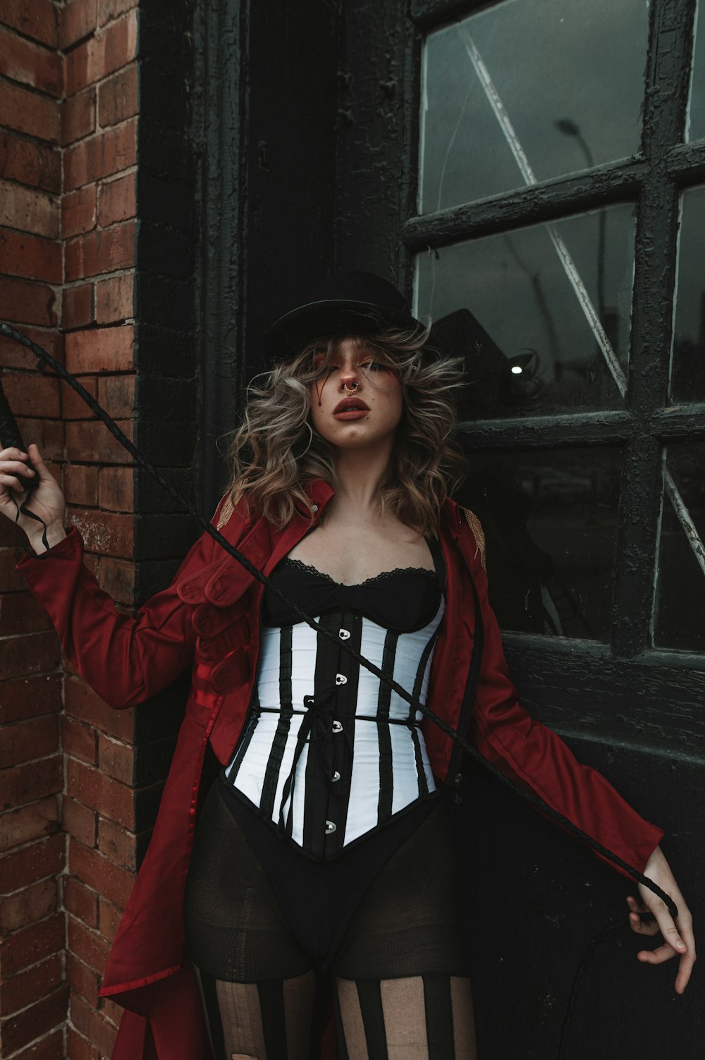 a woman in a corset and hat posing in front of a brick wall
