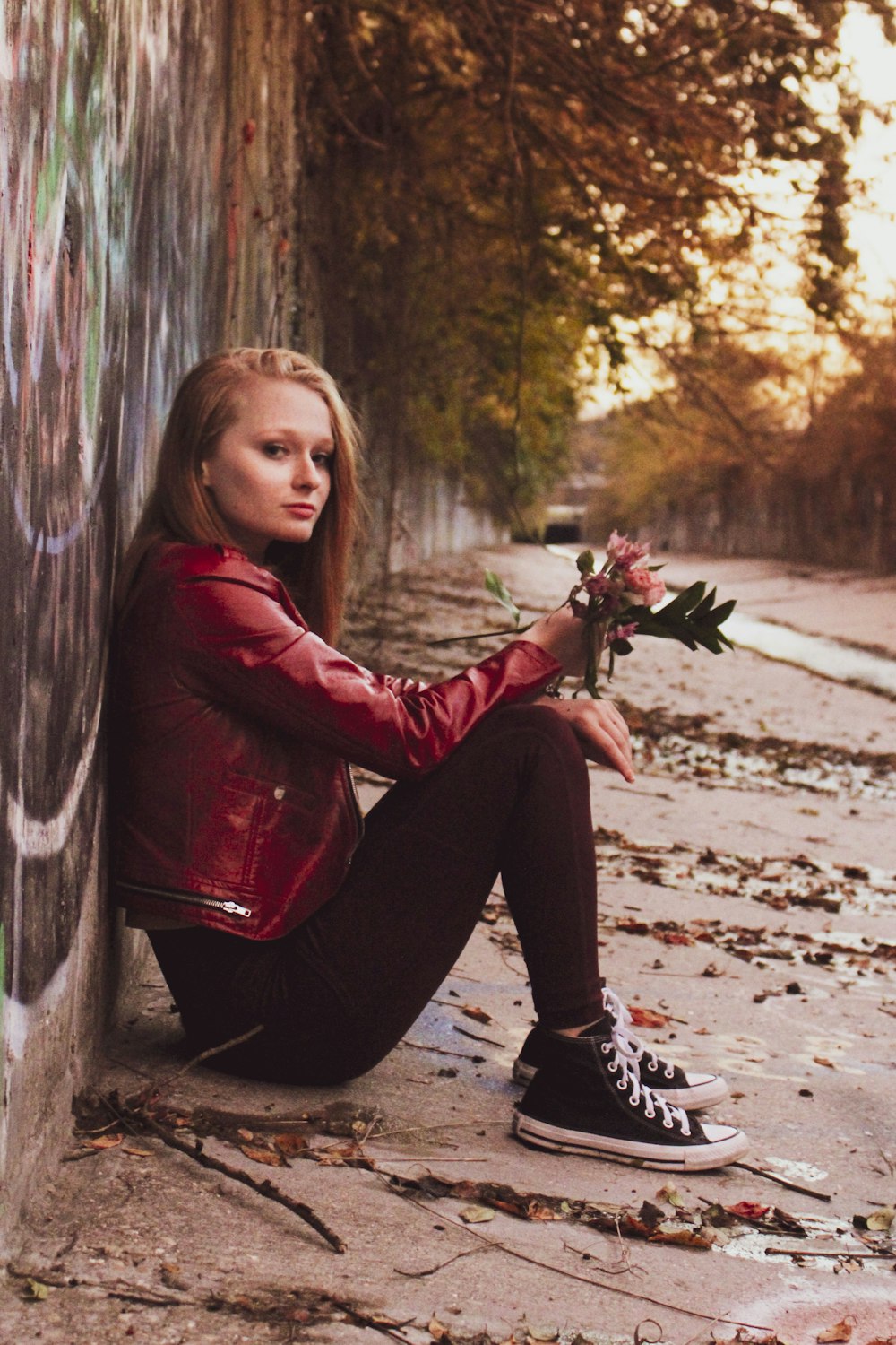 a woman sitting against a wall with a bouquet of flowers