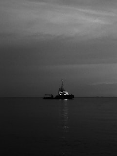Black and white cinematic shot of a ship's prow cutting through calm ocean waters at dawn.