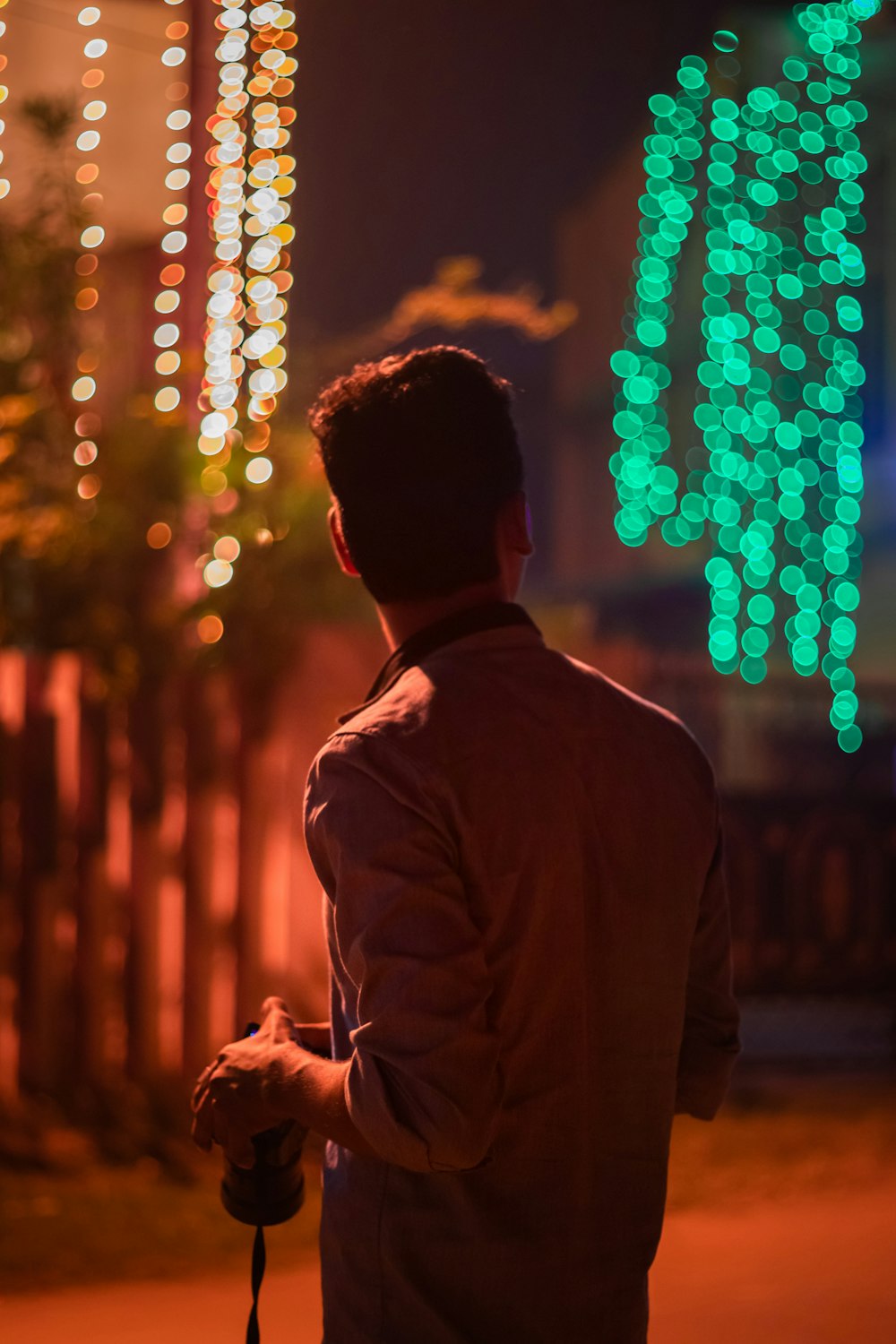 a man standing in front of a fence covered in lights