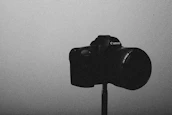 A cinematic black and white photo of a vintage film camera on a tripod in a studio.