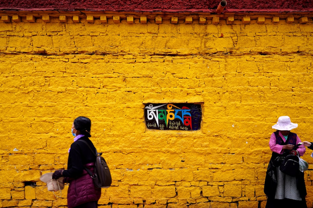 two women standing in front of a yellow wall