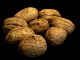 A cluster of uncracked walnuts arranged together against a black background. The surface of the nuts is textured and wrinkled, showcasing their natural brown hues.