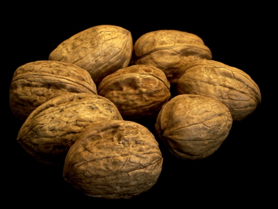 A cluster of uncracked walnuts arranged together against a black background. The surface of the nuts is textured and wrinkled, showcasing their natural brown hues.