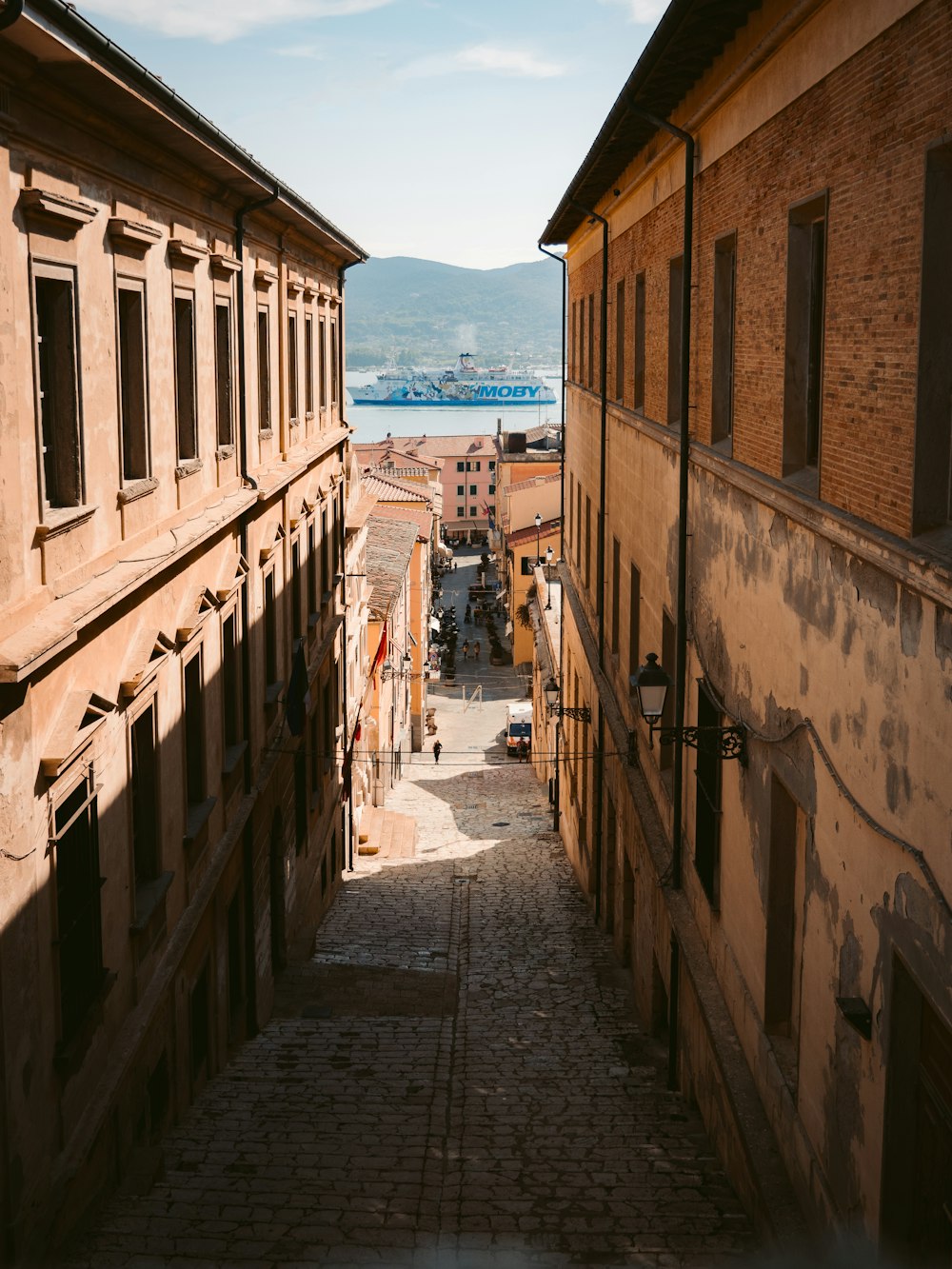a narrow alley way between two buildings with a body of water in the background