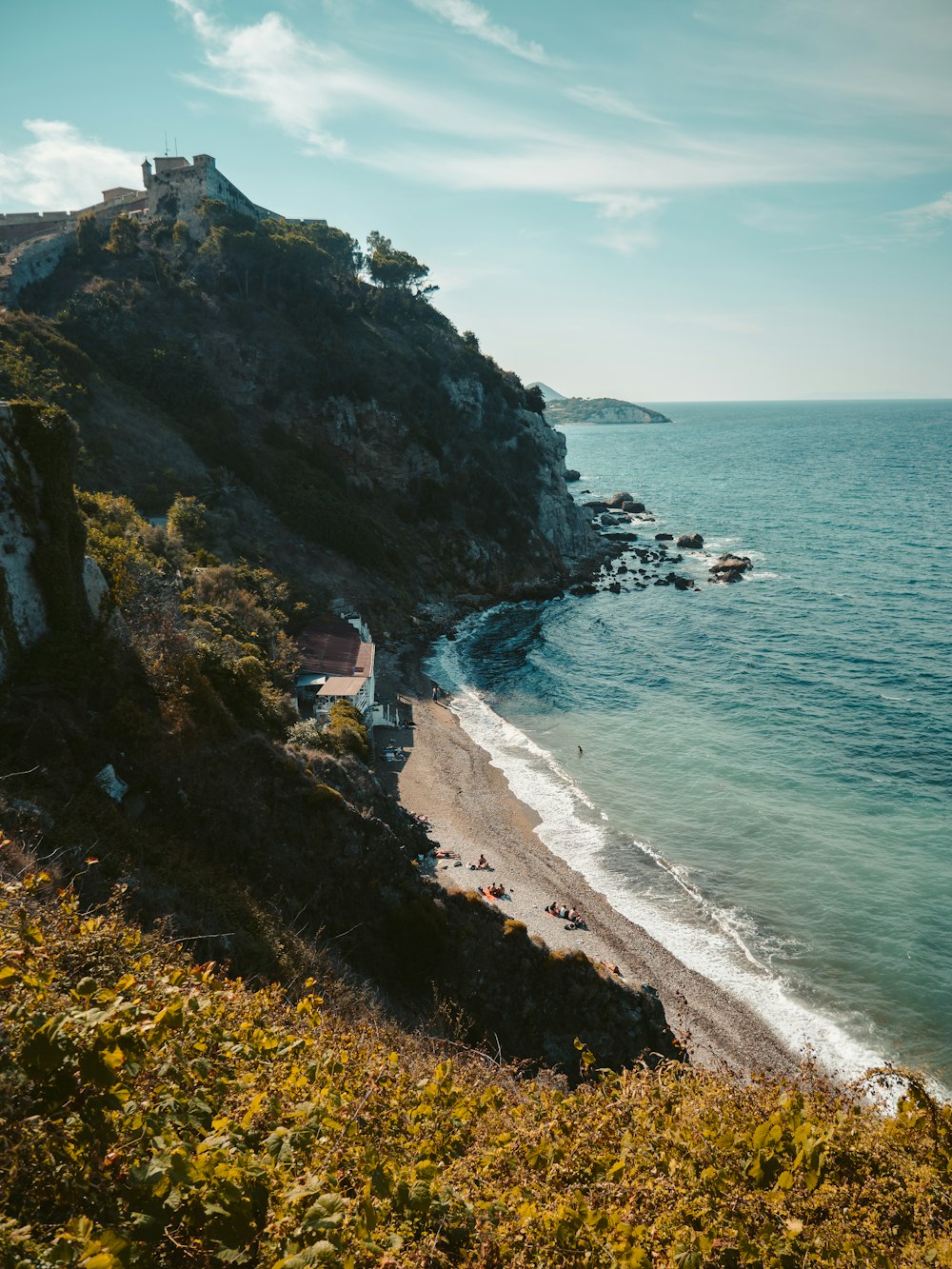 a beach with a house on a hill next to the ocean